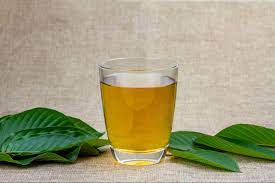 Kratom tea in clear glass with kratom leaves on table around it